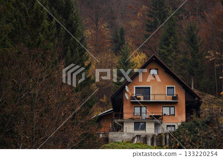Mountain house with warm orange facade and balconies, close view of windows and stucco texture, rural exterior framed by pines Mountain house with warm orange facade and balconies, close view of windows and stucco texture, rural exterior framed by pines 133220254