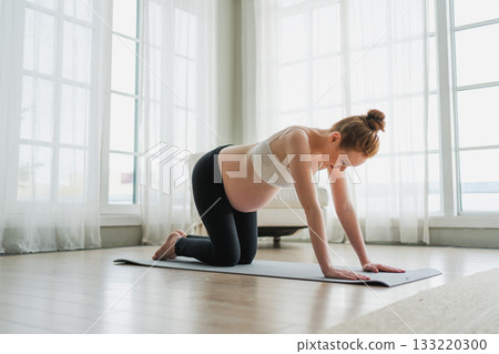 Pregnancy yoga fitness workout training. Pregnant woman practicing yoga at home. Pregnant girl doing sports exercise on yoga mat indoor. Woman with big belly have fitness training practicing asana 133220300