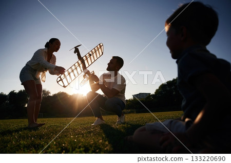Mother, father and son are on field with toy plane, dark colors, dawn 133220690