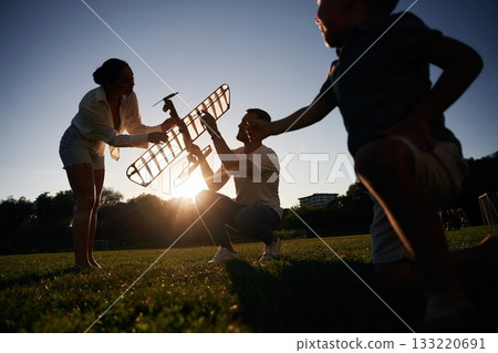 Mother, father and son are on field with toy plane, dark colors, dawn 133220691