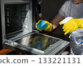A person wearing yellow rubber gloves is cleaning an oven 133221131