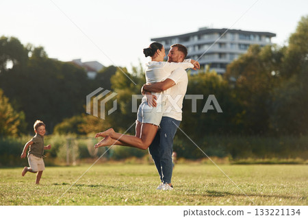 Closeness, embracing. Mother and father are with son outdoors on the field 133221134
