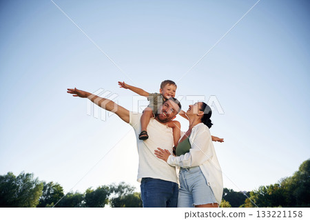 Hands to the sides, flying, imagination. Mother and father are with son outdoors on the field Hands to the sides, flying, imagination. Mother and father are with son outdoors on the field 133221158