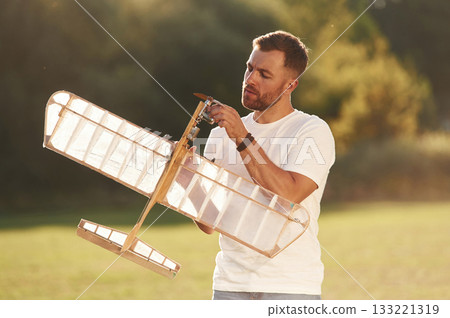 In casual clothes. Man is on the field fixing the toy plane In casual clothes. Man is on the field fixing the toy plane 133221319