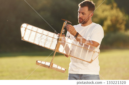 In casual clothes. Man is on the field fixing the toy plane In casual clothes. Man is on the field fixing the toy plane 133221320