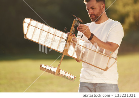 In casual clothes. Man is on the field fixing the toy plane In casual clothes. Man is on the field fixing the toy plane 133221321