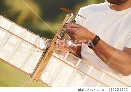 Made of wood. Man is on the field fixing the toy plane Made of wood. Man is on the field fixing the toy plane 133221322