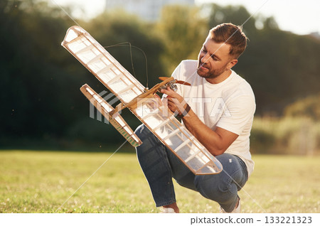 Made of wood. Man is on the field fixing the toy plane Made of wood. Man is on the field fixing the toy plane 133221323