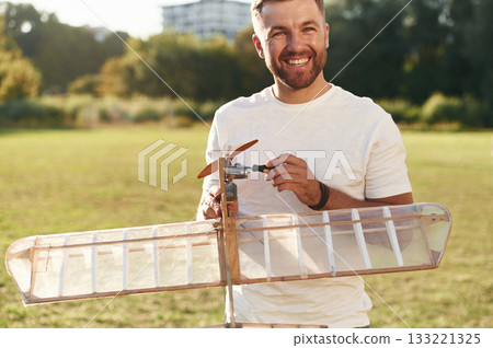 Made of wood. Man is on the field fixing the toy plane Made of wood. Man is on the field fixing the toy plane 133221325