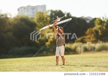 Up in the air, holding it. Cute little boy is playing with toy plane on the field Up in the air, holding it. Cute little boy is playing with toy plane on the field 133221406