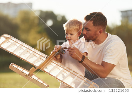 Teaching the kid how to fix it. Father and son are on the field together with toy plane 133221693