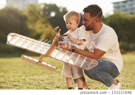 Teaching the kid how to fix it. Father and son are on the field together with toy plane Teaching the kid how to fix it. Father and son are on the field together with toy plane 133221696