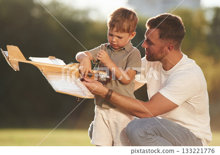 Fixing, using screwdriver. Father and son are on the field together with toy plane 133221776