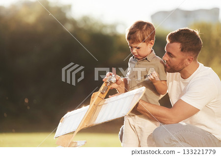Broken, fixing it. Father and son are on the field together with toy plane Broken, fixing it. Father and son are on the field together with toy plane 133221779