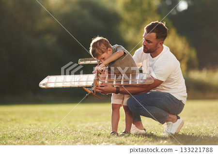 Trying to fix it with screwdriver. Father and son are on the field together with toy plane Trying to fix it with screwdriver. Father and son are on the field together with toy plane 133221788