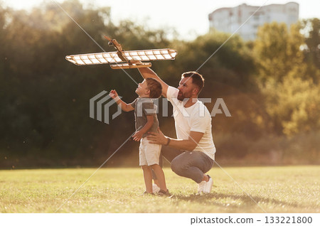 Happy facial expression, fun. Father and son are on the field together with toy plane 133221800