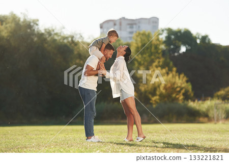 Kid is sitting on the shoulders. Mother and father are with son outdoors on the field Kid is sitting on the shoulders. Mother and father are with son outdoors on the field 133221821