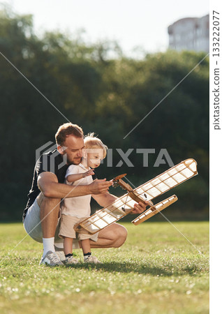 Sitting together. Father and son are on the field with toy plane Sitting together. Father and son are on the field with toy plane 133222077