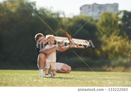 Screwdriver in hand, fixing it. Father and son are on the field together with toy plane Screwdriver in hand, fixing it. Father and son are on the field together with toy plane 133222083