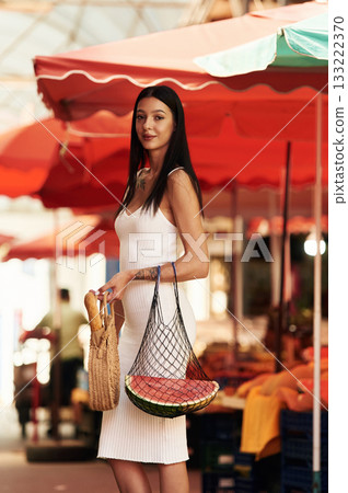Tall young woman is on the vegetable market or bazaar, in white dress 133222370