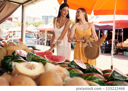 Friend is holding the melon. Two women are together on the marker or bazaar 133222466