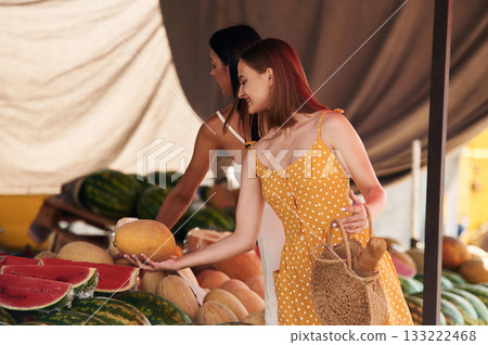 Friend is holding the melon. Two women are together on the marker or bazaar 133222468
