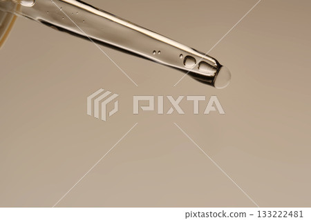 The texture of the serum flowing out of the pipette on a beige background. The texture of the serum flowing out of the pipette on a beige background. 133222481