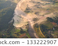Aerial shot of a misty river at sunrise with thick morning fog covering a quiet rural landscape. Scenic countryside view with soft golden light, natural textures, and tranquil atmosphere. 133222907