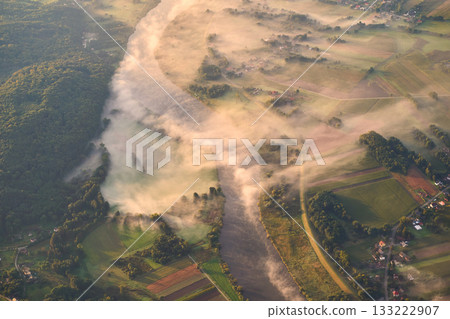 Aerial shot of a misty river at sunrise with thick morning fog covering a quiet rural landscape. Scenic countryside view with soft golden light, natural textures, and tranquil atmosphere. Aerial shot of a misty river at sunrise with thick morning fog covering a quiet rural landscape. Scenic countryside view with soft golden light, natural textures, and tranquil atmosphere. 133222907