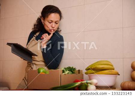 Professional Woman In Apron Reviewing Groceries With Tablet In Modern Kitchen Professional Woman In Apron Reviewing Groceries With Tablet In Modern Kitchen 133223143