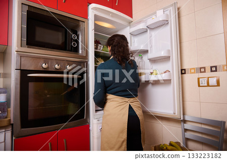 Woman In Kitchen Standing By Open Fridge, Preparing Food Or Shopping Woman In Kitchen Standing By Open Fridge, Preparing Food Or Shopping 133223182