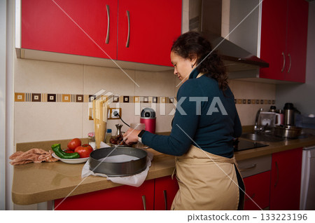 Woman Cooking in Red Kitchen With Apron Preparing Ingredients and Fresh Vegetables Woman Cooking in Red Kitchen With Apron Preparing Ingredients and Fresh Vegetables 133223196