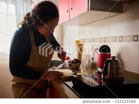 Woman in Apron Chopping on Cutting Board in Cozy Home Kitchen While Cooking 133223198