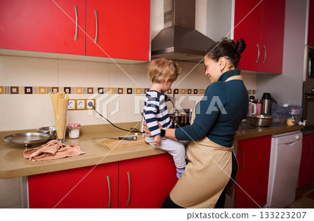 Mother And Child Cooking Together In Bright Red Kitchen With Apron 133223207
