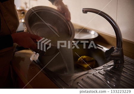 Kitchen Sink Dishwashing Scene With Running Water And Hands Rinsing A Pot 133223229