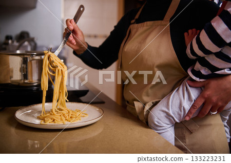 Home Cook in Apron Serving Spaghetti Pasta While Baby Is Held Nearby Home Cook in Apron Serving Spaghetti Pasta While Baby Is Held Nearby 133223231