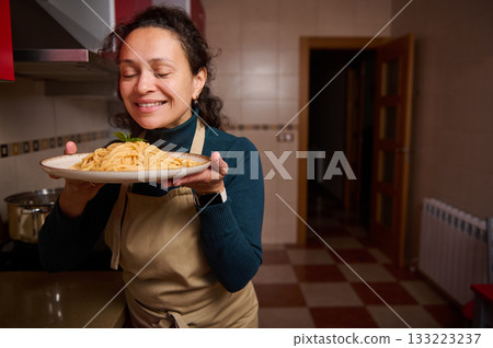 Smiling Woman in Kitchen Presents Plate of Spaghetti, Home Cooking, Happy Dinner Moment Smiling Woman in Kitchen Presents Plate of Spaghetti, Home Cooking, Happy Dinner Moment 133223237