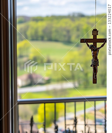 Crucifix hangs from a window, with a view of a green field below 133224017