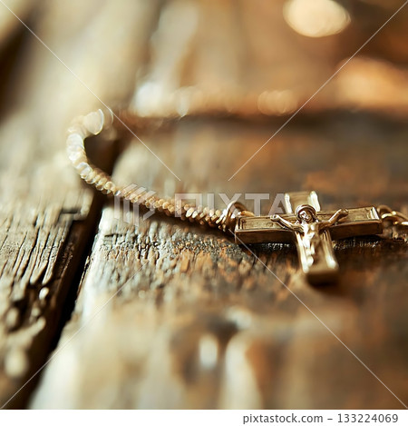 Gold cross necklace with a crucifix on it sits on a wooden surface 133224069