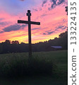 Wooden cross is standing in a field with a beautiful sunset in the background 133224135