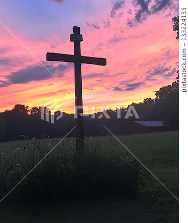 Wooden cross is standing in a field with a beautiful sunset in the background Wooden cross is standing in a field with a beautiful sunset in the background 133224135