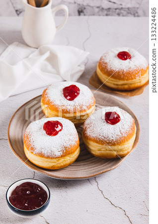 Delicious jam filled donuts with powdered sugar on a plate on the table vertical view Delicious jam filled donuts with powdered sugar on a plate on the table vertical view 133224486