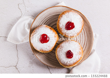 Close up of sweet donuts in powdered sugar with jam on a plate on the table top view Close up of sweet donuts in powdered sugar with jam on a plate on the table top view 133224488