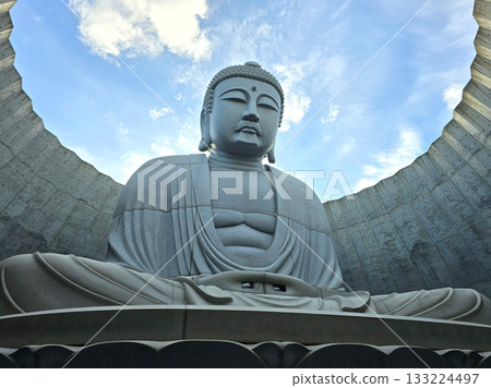 The serene Buddha statue is set against a backdrop of a bright blue sky, creating a sense of peace and tranquility 133224497