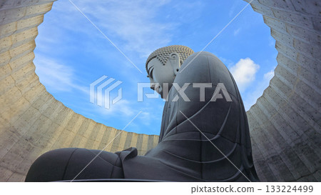 The serene Buddha statue is set against a backdrop of a bright blue sky, creating a sense of peace and tranquility 133224499