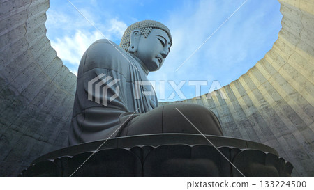 The serene Buddha statue is set against a backdrop of a bright blue sky, creating a sense of peace and tranquility 133224500