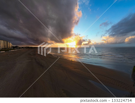 A Dramatic and Breathtaking Sunset Over the Quiet Beach with Majestic Dark Clouds Above 133224754