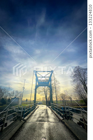 A stunning sunset colors a historic suspension bridge at dusk, creating a magical scene A stunning sunset colors a historic suspension bridge at dusk, creating a magical scene 133224810