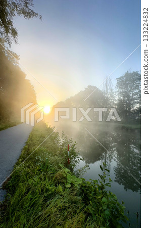 A stunning view of the morning mist gently hovering over calm water during a beautiful sunrise 133224832