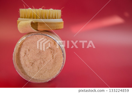 Skincare jar with creamy product and wooden brush on top, set against a bright red background, highlighting beauty and self-care routines 133224859